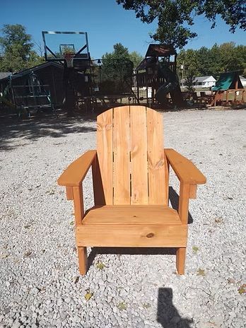 Wooden Adirondack chair outdoors on gravel.