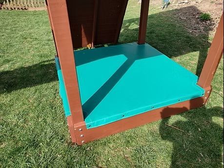 Green sandbox with brown wooden frame, set on grass.