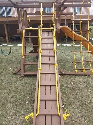 Playground with wooden ramp, ladder, and slide. Yellow ropes border the ramp.