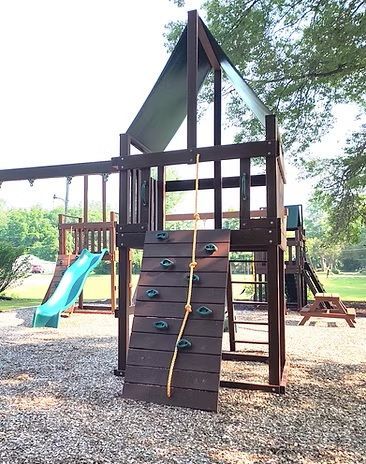 Playground with brown wooden structure, rock wall, rope, slide, and picnic table.