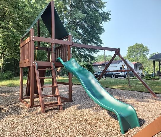 Playground with wooden structure, green slide, swing set, and wood chip ground.