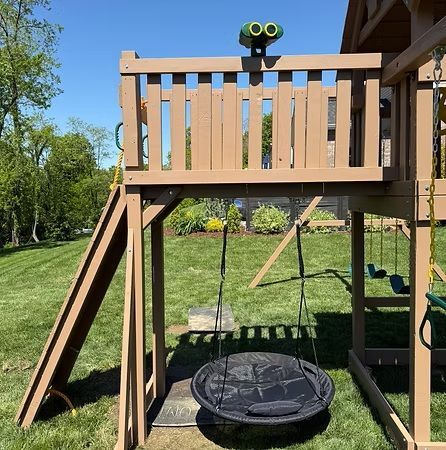 Playground with slide, swings, and lookout deck in a grassy yard under a blue sky.