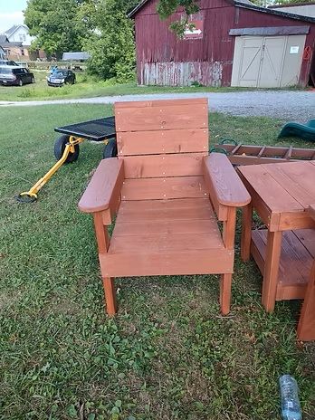 Wooden chair and side table on a grassy lawn; a red barn and other structures in the background.