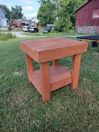Wooden, reddish-brown side table in a grassy yard, with a lower shelf.