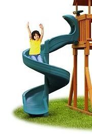 Girl on a green spiral slide at a playground, arms raised, smiling.