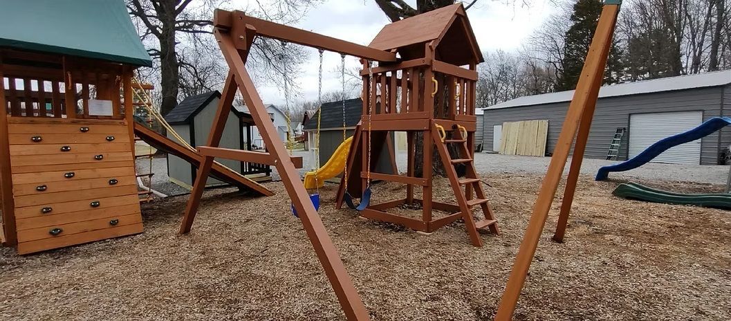 Wooden playground equipment in a yard with swings, slide, climbing wall, and a playhouse.