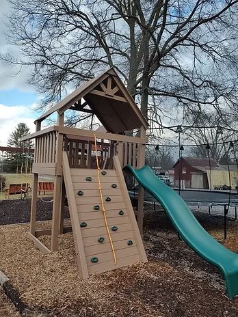 Play structure with a climbing wall, slide, and wooden roof.
