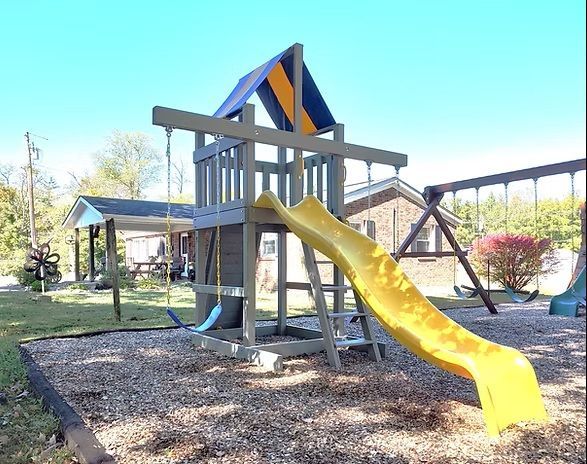 Playground with gray wooden structure, yellow slide, swings, and blue and yellow roof under a blue sky.