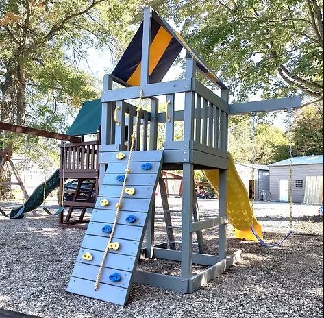 Wooden playground structure with climbing wall, slide, and rope ladder.