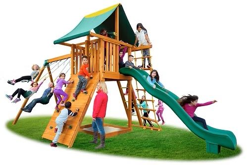 Children playing on a wooden playground with a slide, swings, and climbing wall.
