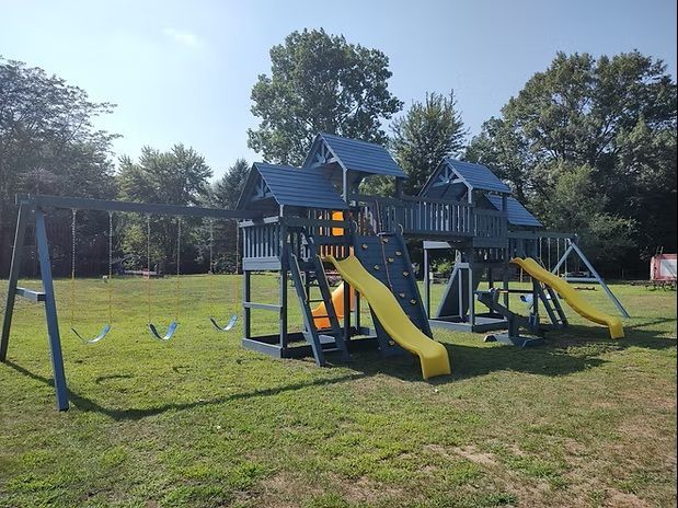 Playground with swings, slides, and climbing structures on a grassy area, under a blue sky.