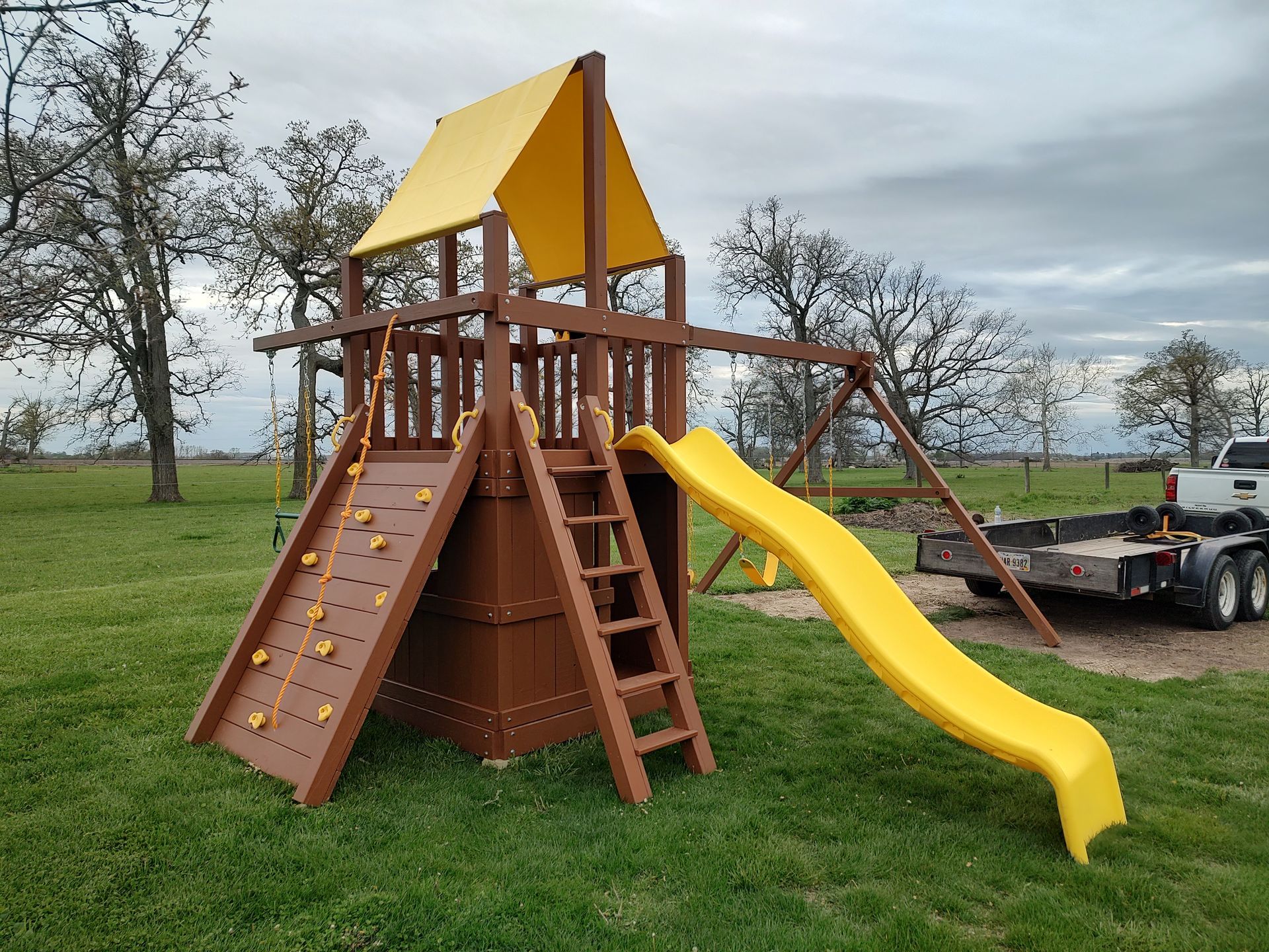 Wooden playset with climbing wall, slide, and swing set in a grassy backyard.
