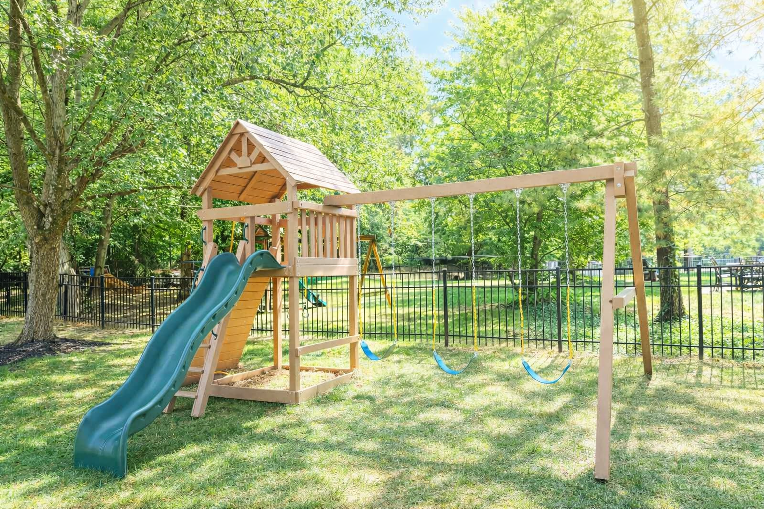 Wooden playground structure with a slide, swings, and roof in a grassy backyard.