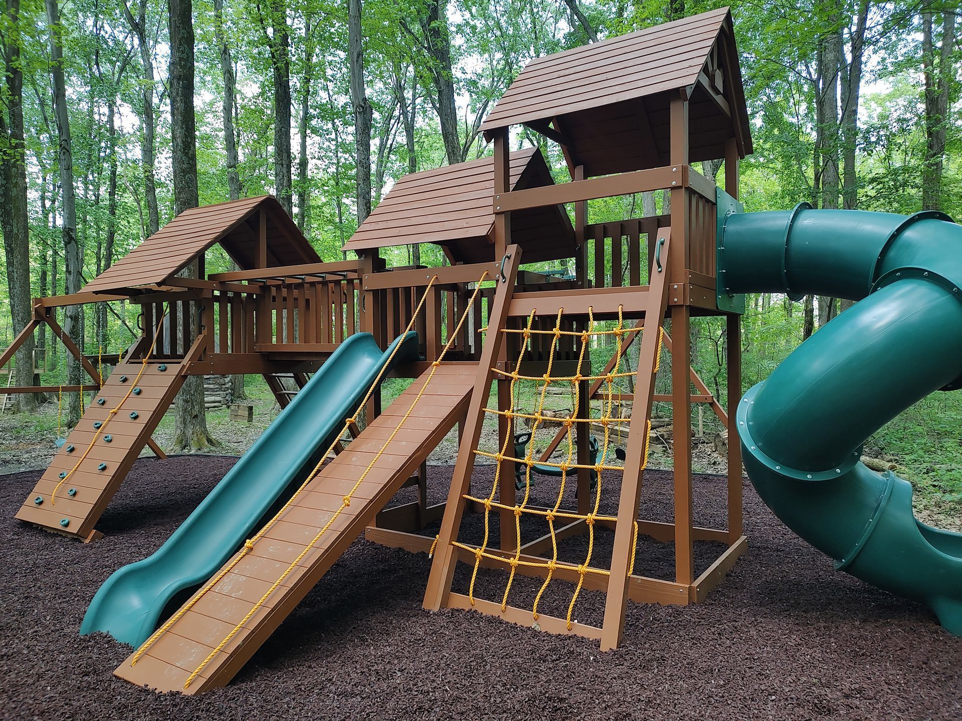 Wooden playground with slides, rope net, and climbing structures in a wooded park