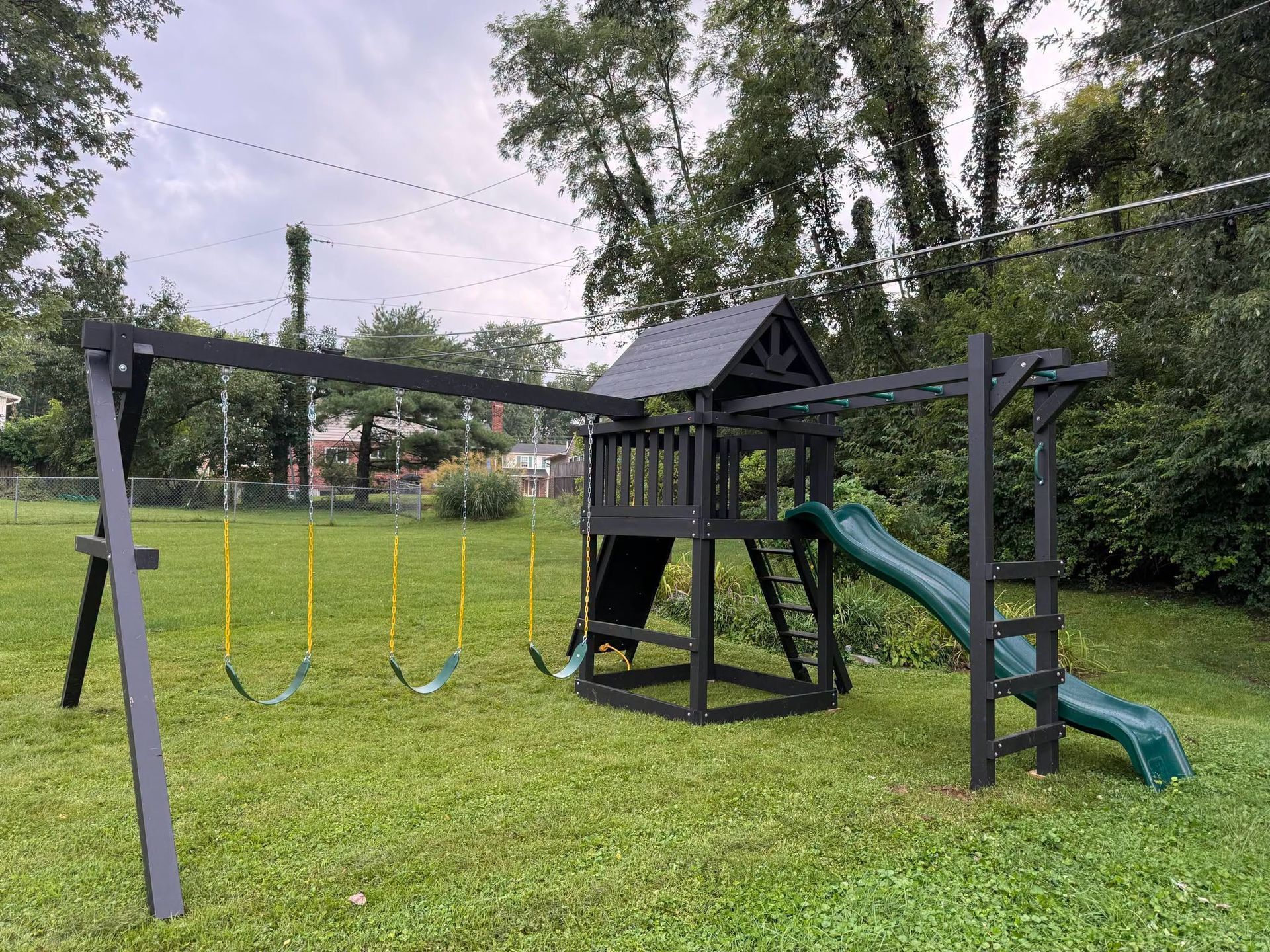 Backyard playground set with swings, climbing tower, and green slide on a grassy lawn