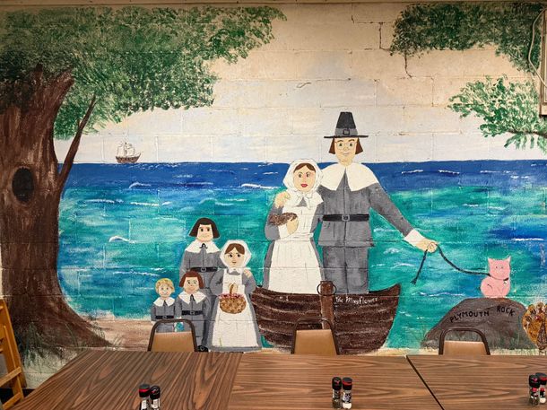 A painting of a pilgrim family on a boat in front of the ocean.