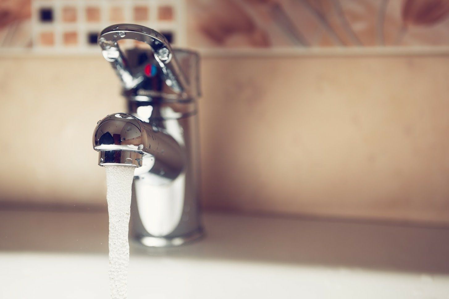 A shiny chrome faucet pouring a steady stream of water into a sink.