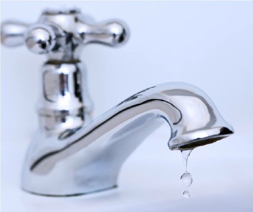 A shiny chrome bathroom faucet against a white background, with a single water droplet falling from the spout.