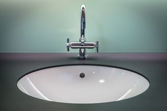 A chrome faucet mounted on a dark grey countertop above an oval white bathroom sink.