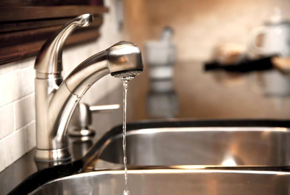 A sleek, stainless steel kitchen faucet with a pull-down sprayer head dispensing a thin stream of water into a metal sink.