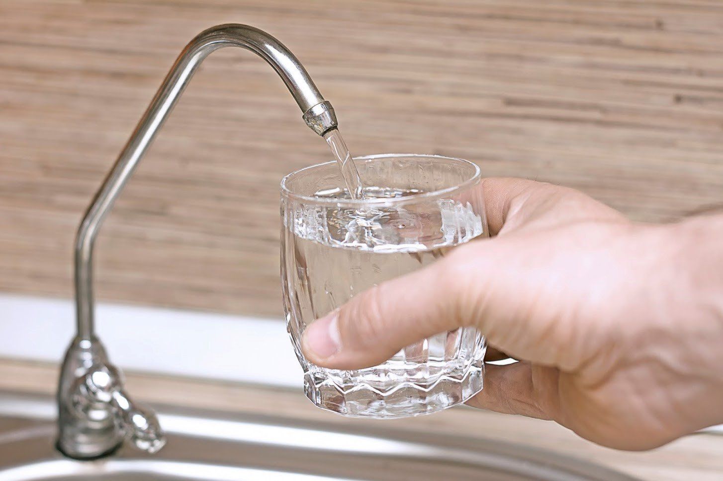 A hand holds a glass under a metal faucet, filling it with clear water.