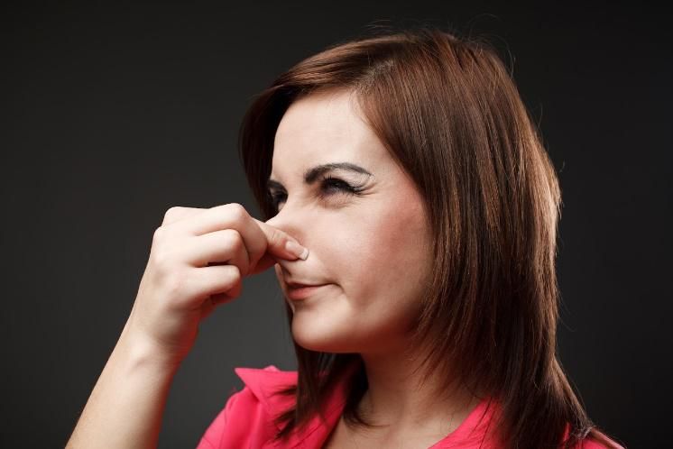 A person wearing a pink shirt pinches their nose shut with one hand, making a pained expression against a dark background.