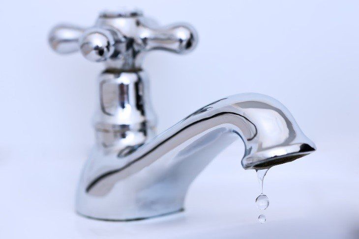 A chrome faucet against a plain white background, with water dripping from the spout.