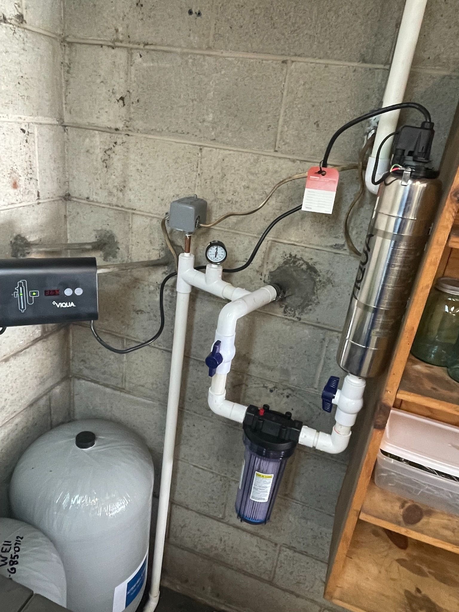 A residential water treatment and filtration system mounted on a concrete wall, including a pressure gauge and tank.