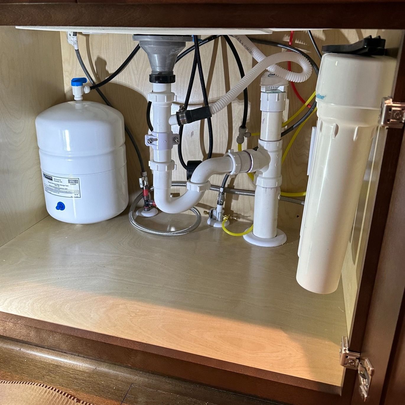 An under-sink reverse osmosis water filtration system featuring a white storage tank and a vertical filter canister.