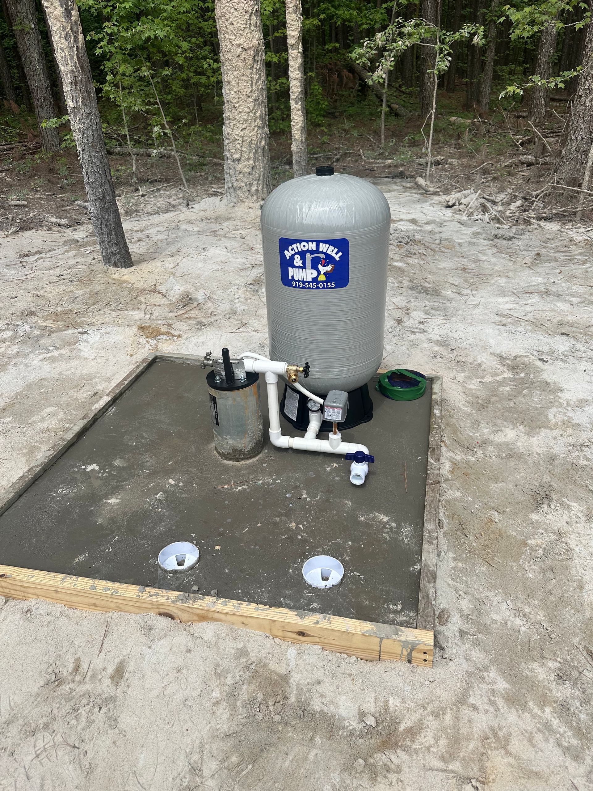 Outdoor utility tank and pump on a concrete pad in a wooded area.