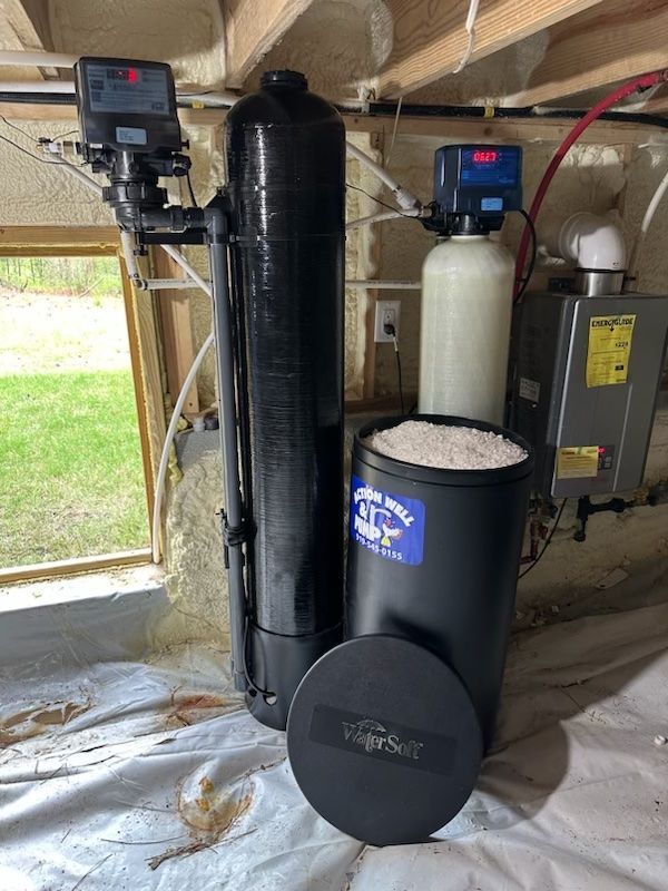 Water softener and filtration tanks installed under a house, with a black tank and control units.