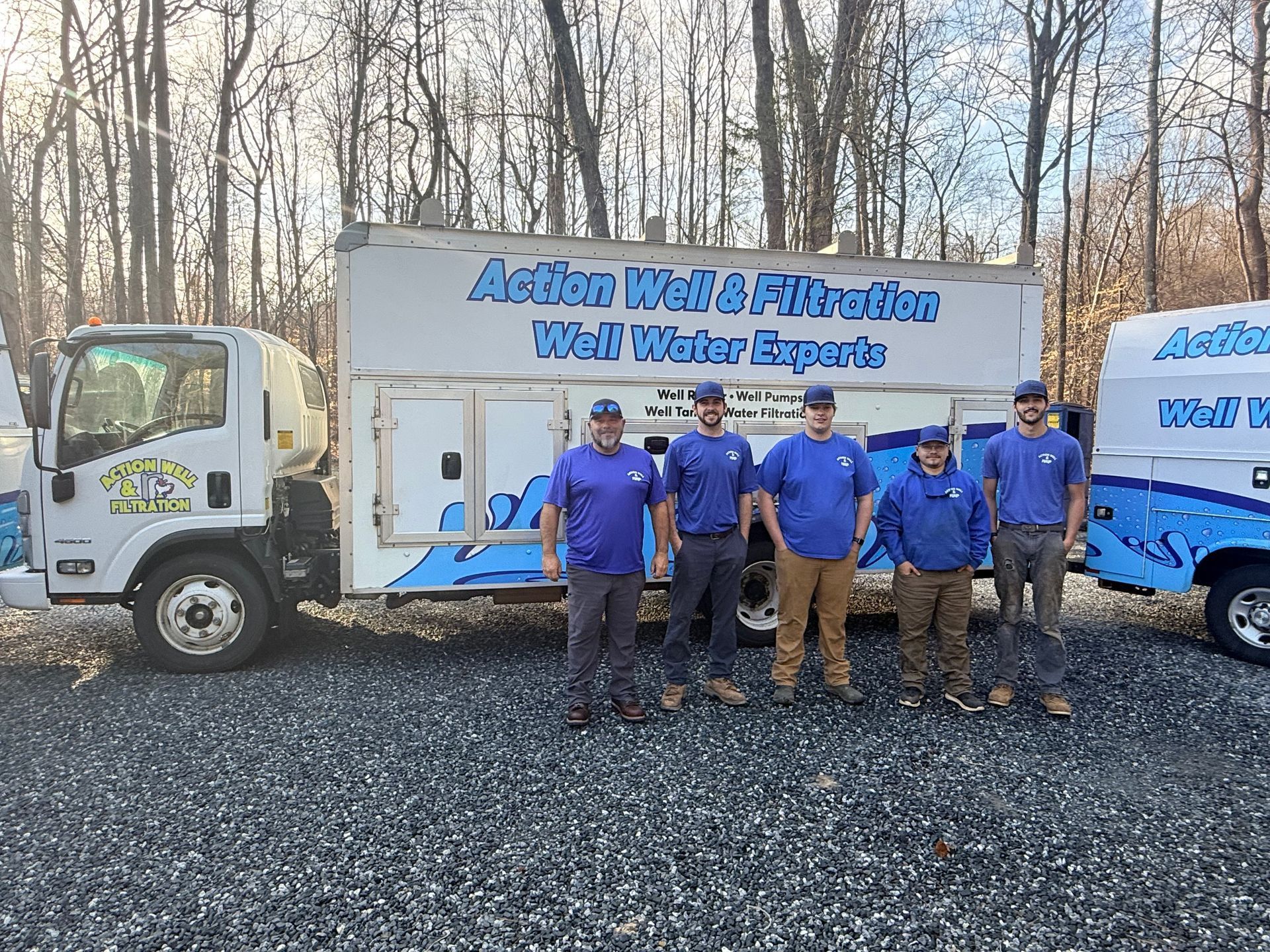Five workers in blue shirts posing beside a white Aqua Well & Pump service truck on gravel