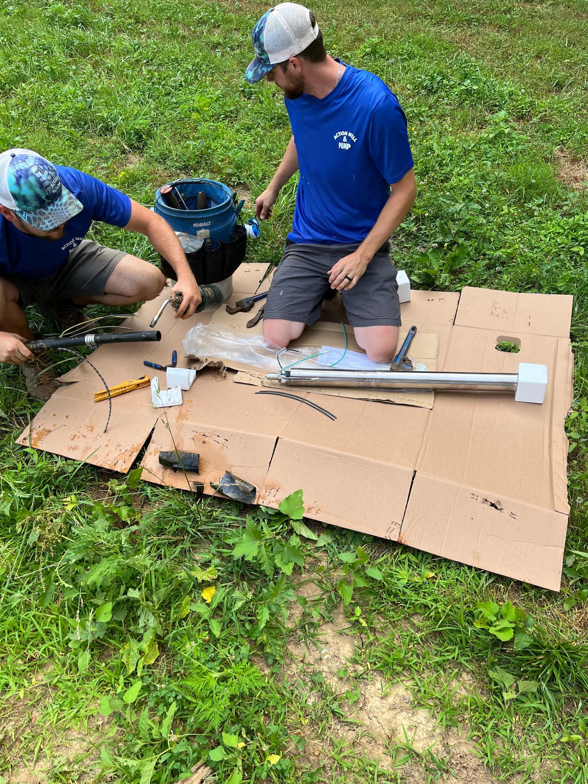Two people assembling a large white model on cardboard in a grassy outdoor area