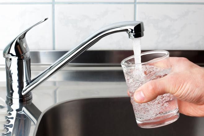 A hand holds a glass under a kitchen faucet as it fills with running tap water.