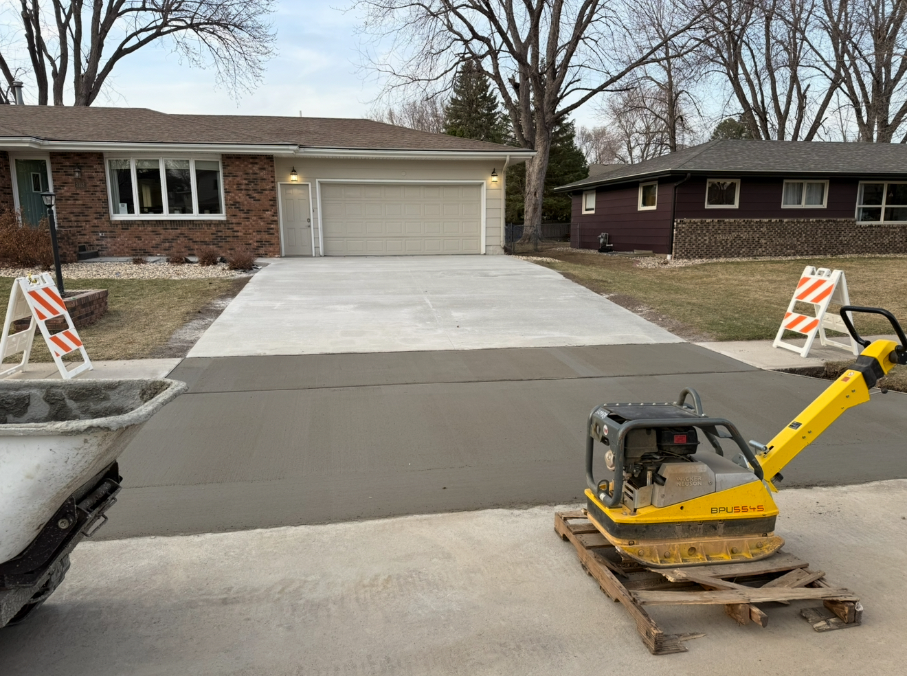 Newly poured concrete driveway at a house, with construction equipment and warning signs.