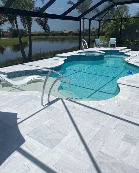 Swimming pool with white deck tiles, surrounded by a screen enclosure and overlooking a lake.