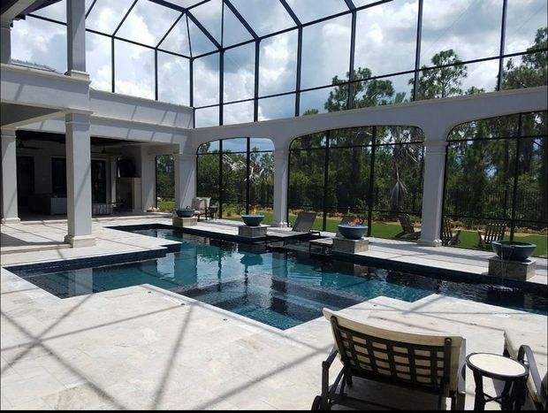 Pool area with screened enclosure and trees in the background. Two lounge chairs are visible in foreground.
