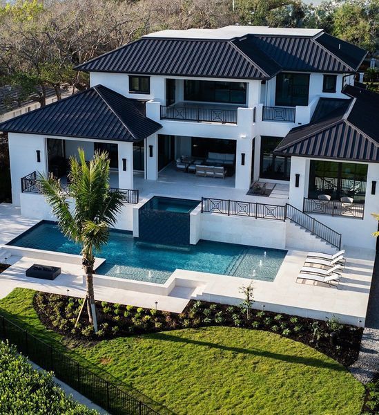 Modern white house with dark roof, pool, and manicured lawn.