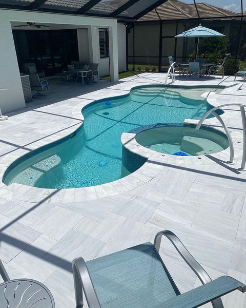 Pool and spa with light blue water and surrounding white tile patio.