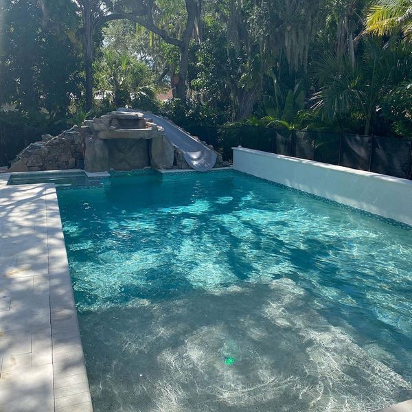 Swimming pool with a water slide surrounded by trees.