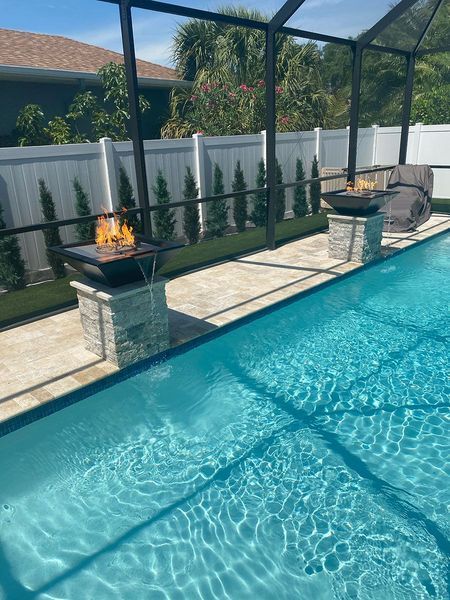 Swimming pool with two lit fire pits on stone columns, under a screened enclosure.