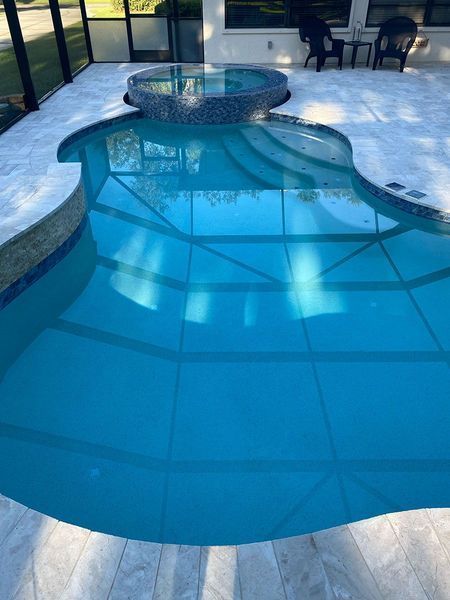 Pool with jacuzzi, blue water, light-colored tile surround.  Glass enclosure, outdoor setting.