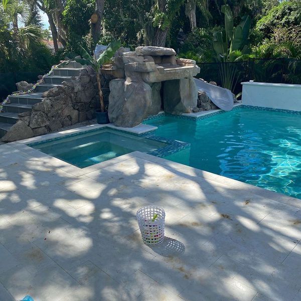 Swimming pool with waterfall feature and slide, concrete deck, and stairs.