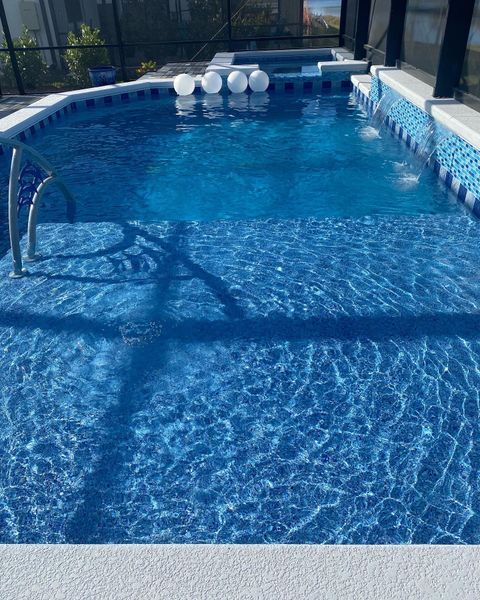 Swimming pool with blue tile and water. White floats rest on surface. Sunlight creates shadows.
