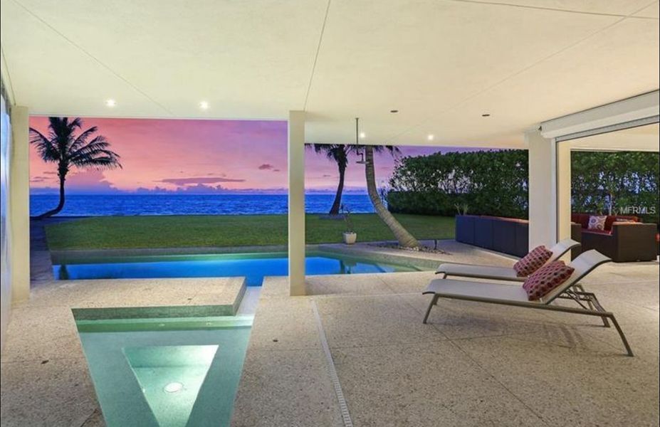 Patio overlooking pool and ocean at sunset, with palm trees and lounge chairs.