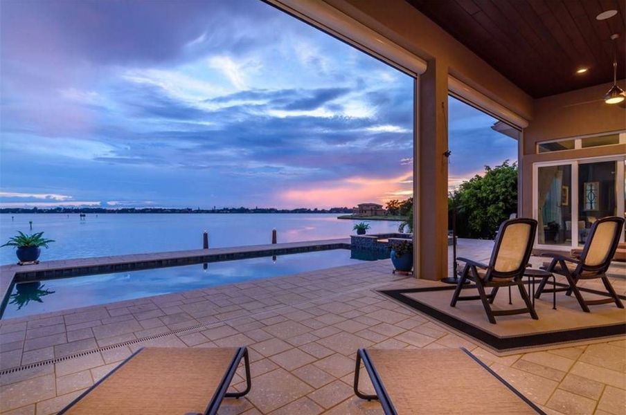 Patio overlooking water and pool at dusk with lounge chairs.