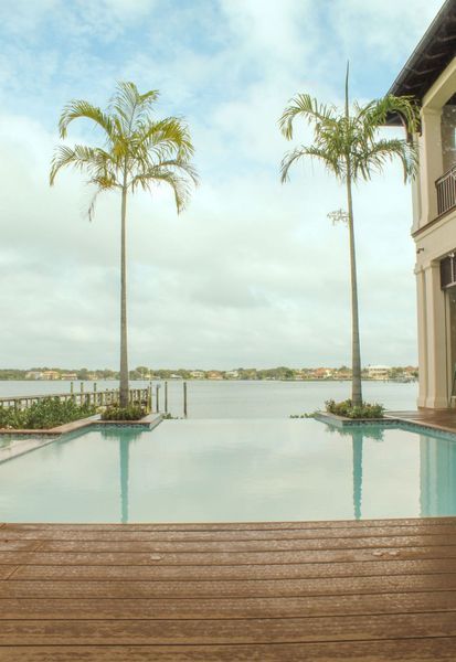 Infinity pool with palm trees, overlooking a lake, adjacent to a large building.
