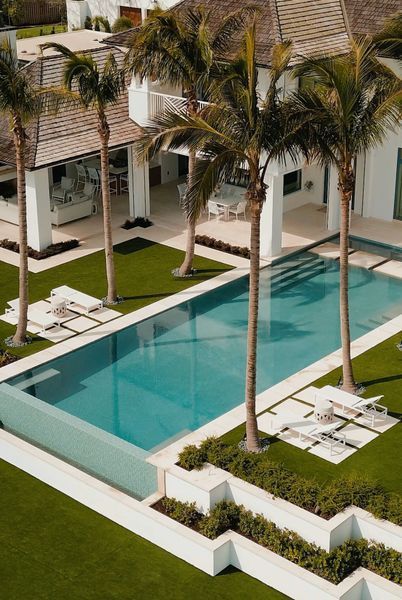 Luxurious home with pool, palm trees, and manicured green lawn. White exterior.