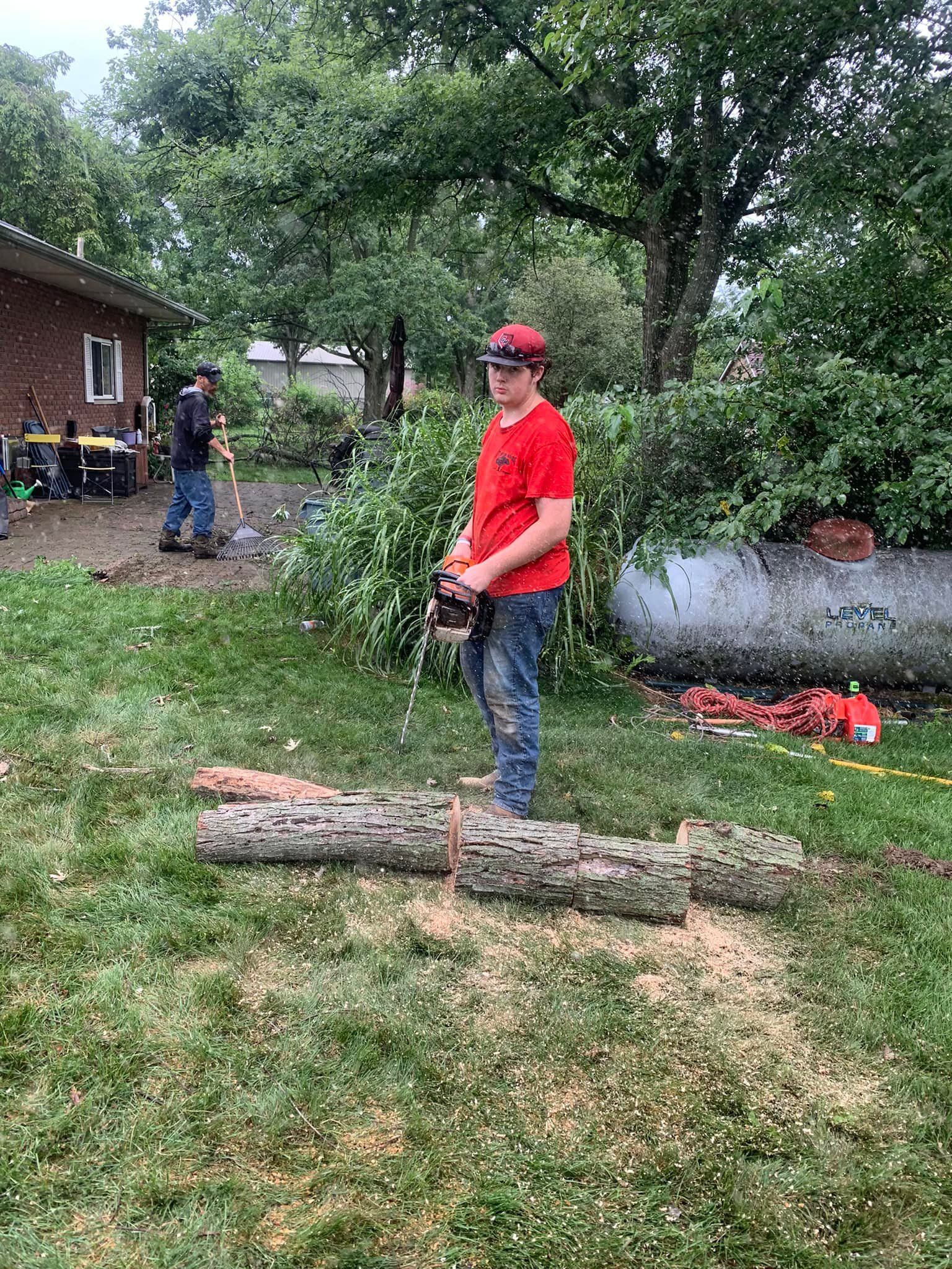A man is standing next to a large log in a yard.