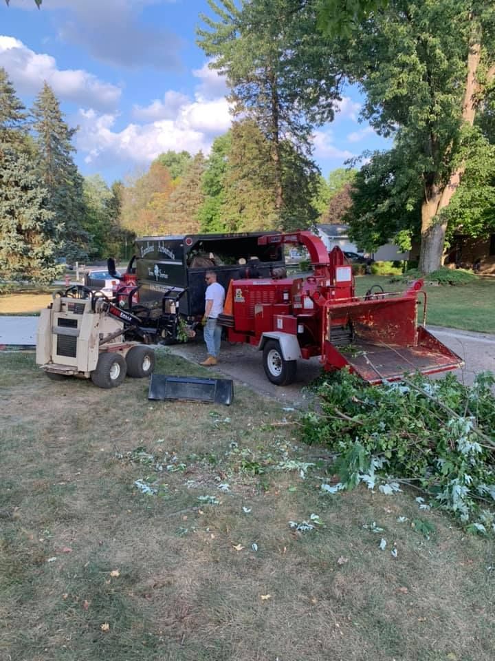 A man is standing next to a tree chipper in a yard.
